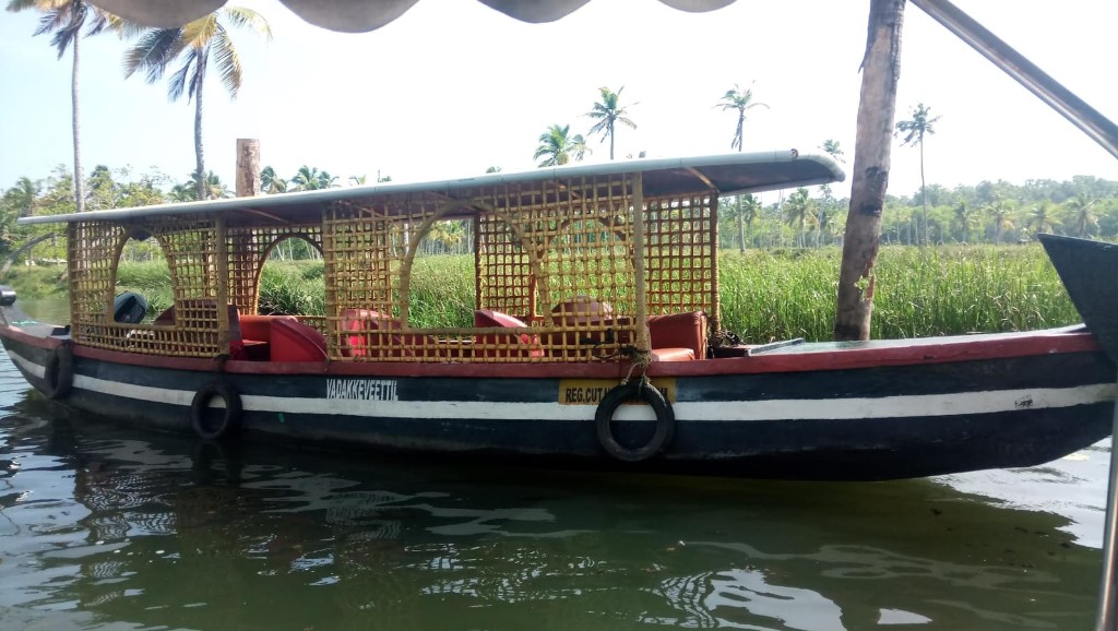 Traditional Kerala tour boat with red seats on the Poovar backwaters, surrounded by palms and reeds